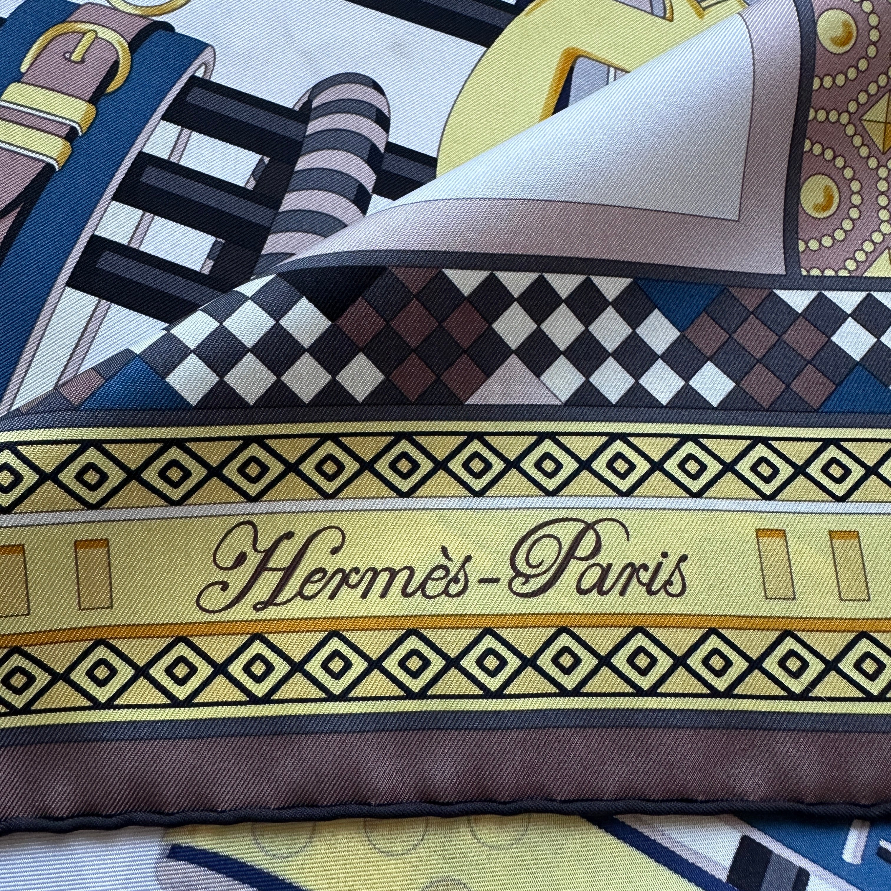 Signature "Hermès-Paris" en bas du foulard sur bordure à damiers.