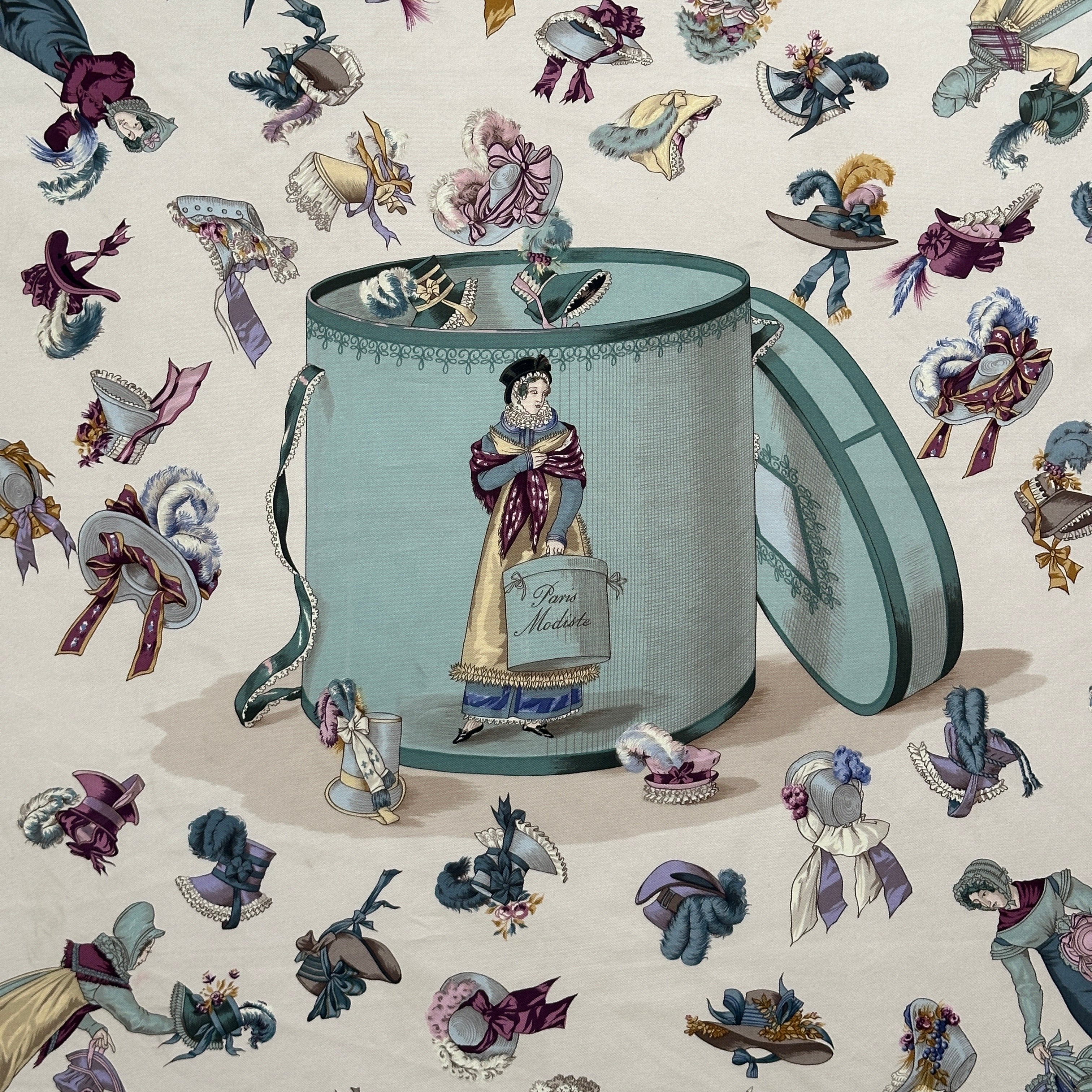 Détail du motif central : une modiste parisienne debout dans une grande boîte à chapeaux bleue, tenant un carton "Paris Modiste".